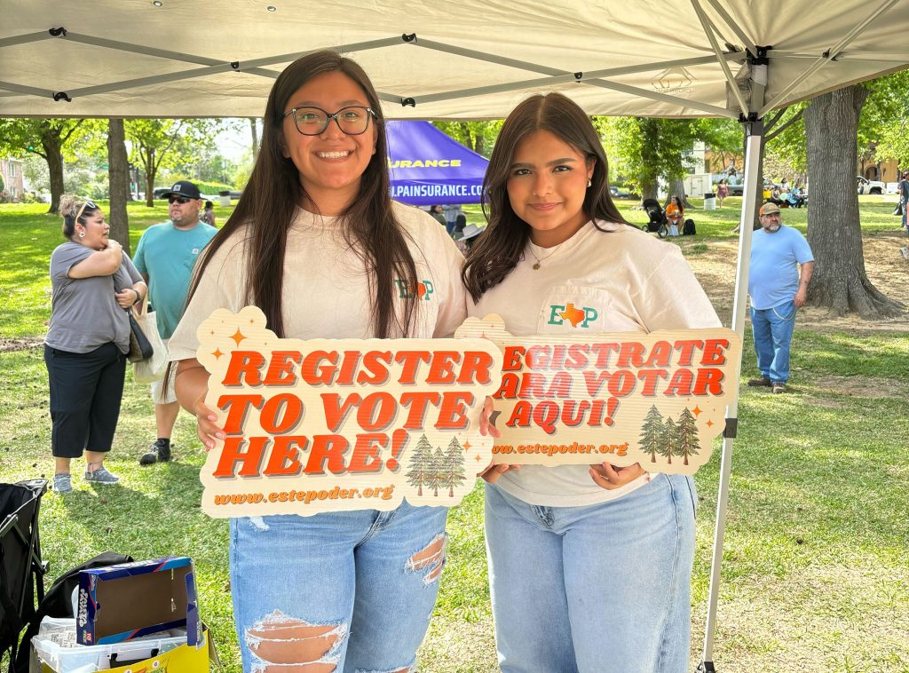 Two women stand together with signs that read "Register to Vote"