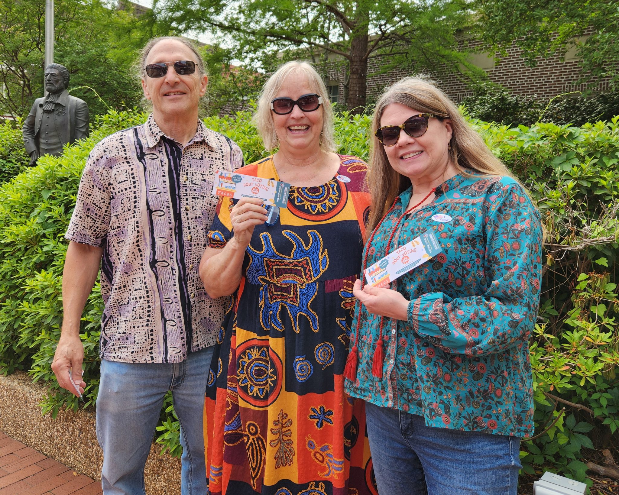 Three people stand together and hold up paper tickets